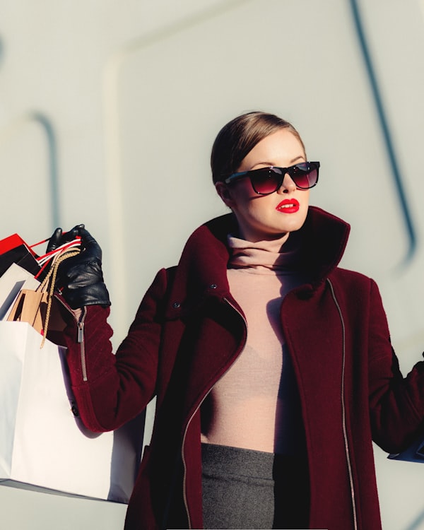 Model in a burgundy coat and sunglasses, shopping bags in hand