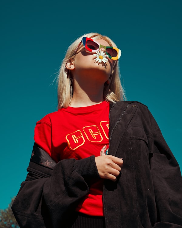 Model in a red T-shirt looking up at a blue sky, a daisy between her lips